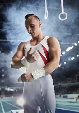 Male gymnast wrapping wrists below gymnastics rings in arena Stock Photos