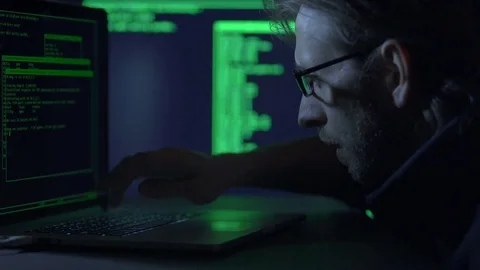 Male hacker or programmer working on a laptopi in a dark office room Stock Footage 71221372
