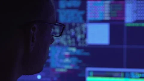Male hacker working on a computer in a dark office room. Foto stock