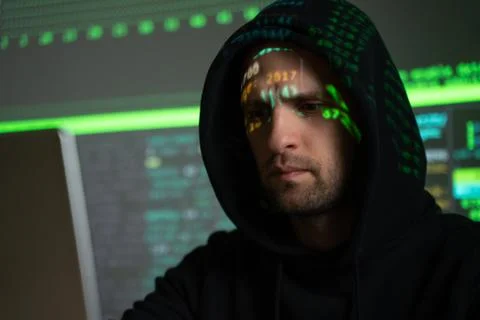 Male hacker working on a computer while green code characters reflect on his 写真素材