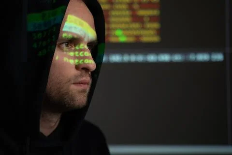 Male hacker working on a computer while green code characters reflect on his Stockfoto's