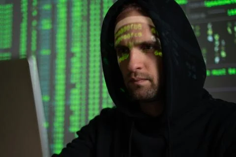 Male hacker working on a computer while green code characters reflect on his Foto stock