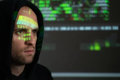 Male hacker working on a computer while green code characters reflect on his 스톡 사진