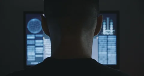 Male hacker works on a computer with maps and data on display screen in dark Stock Footage 95703614