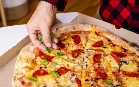Male hand adding basil leaves to pizza Stock Photos