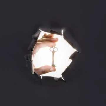 Male hand breaking through the gray paper background and holding key 스톡 사진