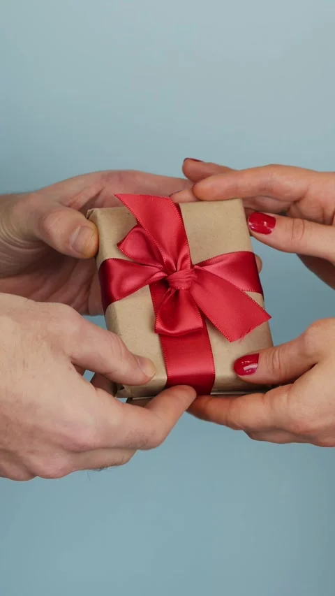 Male hand giving present gift with red ribbon bow to female hand. Vertical video Stock Footage 296894111