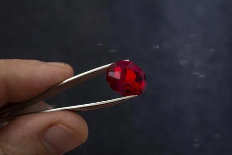 Male hand holding a red ruby with a sharp tweezers on black glitter backgro.. 스톡 사진