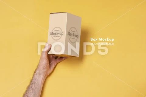 Male hand holding a small box in front of yellow background mock-up series PSD Template