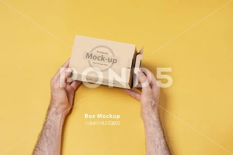 Male hand holding a small box in front of yellow background mock-up series PSD Template