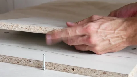 A male hand inserting a fastener element into wooden furniture and hammering it Stock Footage 247152481