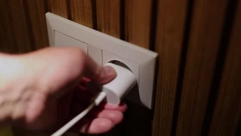 Male hand inserts mobile phone charger plug in white wall socket Stock Footage 309964338