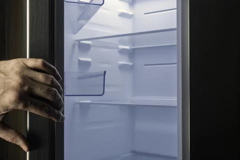Male hand opens clean empty refrigerator with cold blue light, symbolizing ne Stock Photos