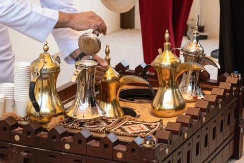 Male hand opens silver dallah lid on sand heater to prepare spiced drink. tra Stock Photos