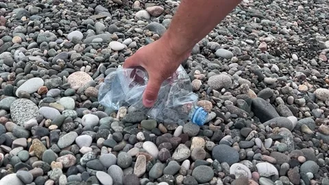 Male hand picking up empty squeezed plastic water bottle from pebble beach Stock Footage 332560904