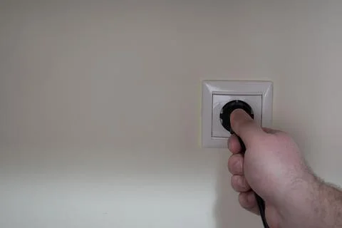 A male hand is pulling one black electrical cord plugged into a wall socket Stock Photos