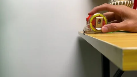 Male hand pulling roll of measuring tape on wooden table indoor office room Stock Footage 249375453