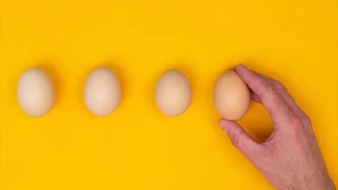 Male hand pulls gradient of eggs, on yellow background, top view Stock Footage 128926564