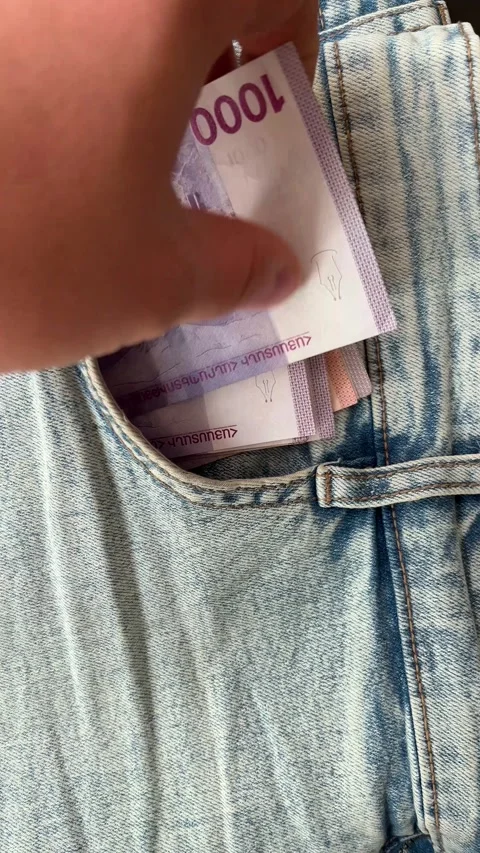 Male hand pulls of stack of 1000 dram into pocket of blue denim jeans pants Video stock 343801272