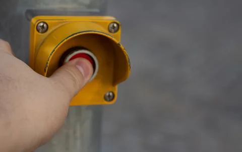 Male hand pushing red button in yellow box on pole on pedestrian crossing Stock Photos