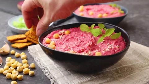 Male hand puts chips in ceramic bowl of hummus with beet. Stock Footage 127058834