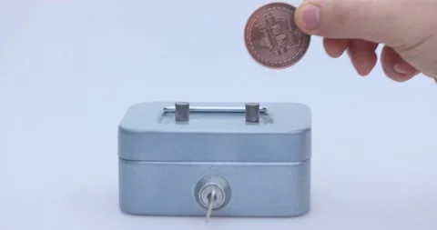 Male hand puts a cryptocoin, Bitcoin or BTC, in a small grey vault, safe or Vídeos de archivo 166241356