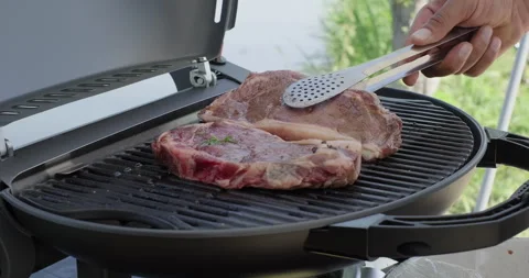 Male hand puts raw beef steak on a grill. Picnic party outdoors. Backyard BBQ Stock Footage 276818116