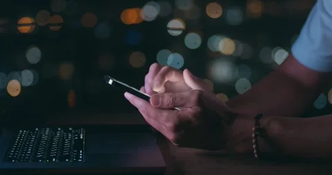 Male hand scrolling browsing on mobile phone at night time while working at Stock Footage 241560927