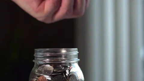 Male hand sideways angle drops coins into jar. Stock-Footage 69944904