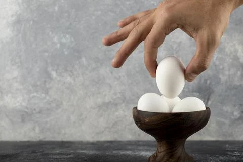 Male hand taking raw egg from wooden bowl Stock Photos
