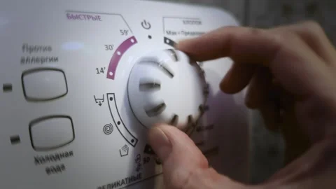 Male hand turns timer knob for wash programs on washing machine. Selecting cycle Stock Footage 340386657