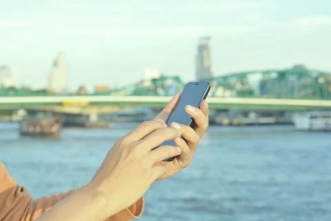 Male Hand using Mobile Smart Phone near the iron bridge in Bangkok as wireles Stock Photos