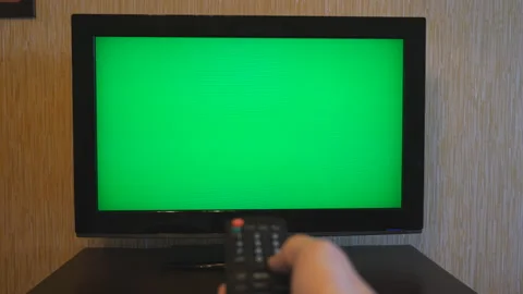 Male hand using a remote control to flipping channels on green screen TV. Arm of Stock Footage 87987229