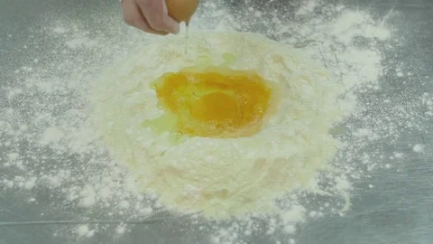 Male hands break a raw egg into flour. Dough preparation process slow motion Stock Footage 74716122