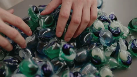 Male hands carefully sorting through pile of colorful laundry detergent capsules Stock Footage 312352558
