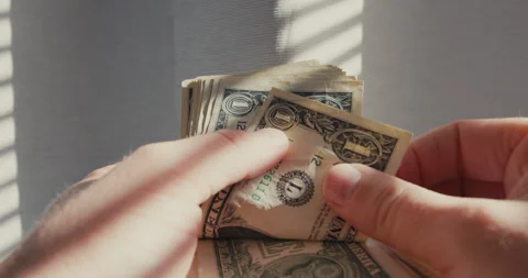 Male hands counting a stack of American one dollar bills in bright sunlight from Video stock 347010069