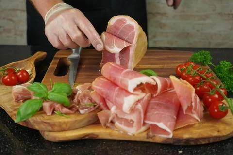 Male hands cutting with sharp knife traditional Spanish dry smoked ham leg Stock Photos
