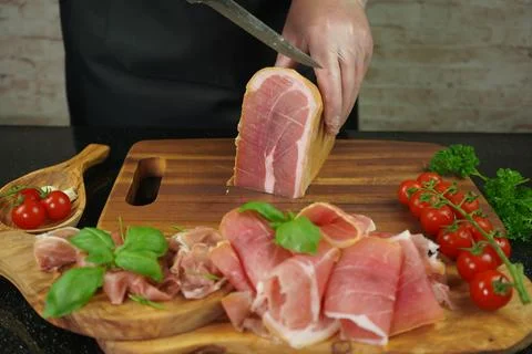 Male hands cutting with sharp knife traditional Spanish dry smoked ham leg Stock Photos