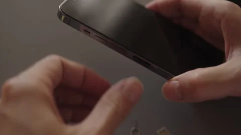 Male hands inserting sim card ejector tool into smartphone, replacing or Stock Footage 323203652
