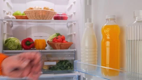 Male hands put a bottle of orange juice in the fridge with vegetables Stock Footage 260769887