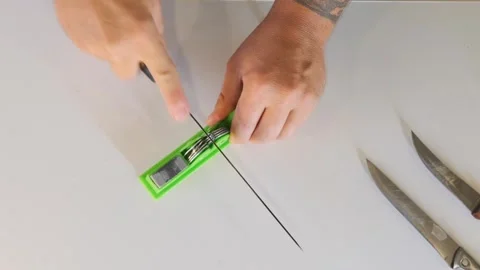 Male hands sharpening kitchen knife on manual sharpener top view on table Stock Footage 333765090