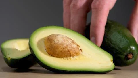 Male hands stack one natural whole avocados on the table next to the cut avocado 스톡 사진