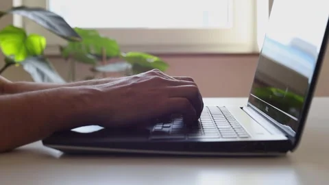 Male hands typing on a laptop at a table near the window Stock Footage 244599127