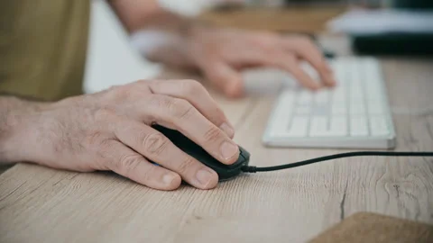 Male hands using a computer mouse with a keyboard in soft focus, conveying Stock Footage 333722143