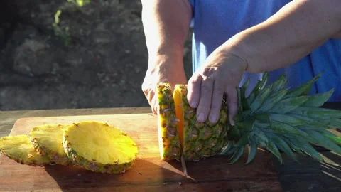 Male hands using a sharp knife to cut a fresh, juicy tropical pineapple into Vídeos de archivo 341832525