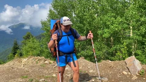 Male hiker walking in front view with loaded backpack and trekking poles Stock Footage 343773449