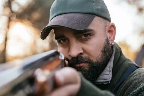 Male hunter looking at the camera while aiming a gun at his prey. Stock Photos