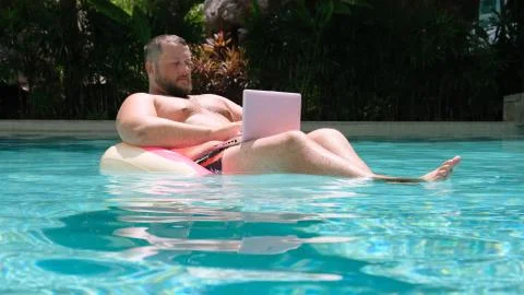 Male with an inflatable ring in the water in the pool works on the computer Stock Photos