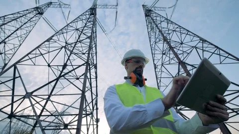 Male inspector is operating a computer in front of ETL towers in slow motion Stock Footage 101200520