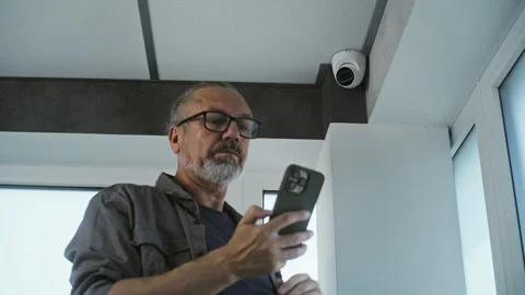 Male installer adjusts security camera using application on smartphone Stock Footage 280844131